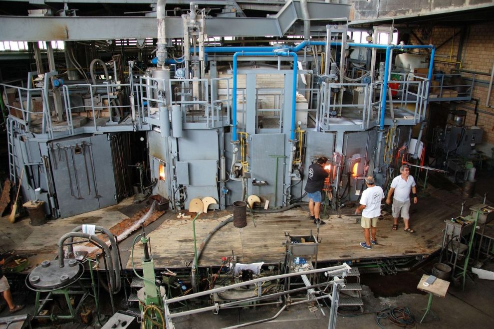 Modern industrial kiln facility with workers operating high-temperature ceramic processing equipment.