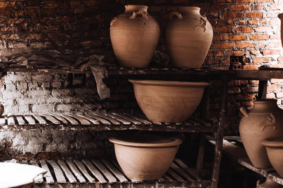 Unfired clay pots drying on wooden shelves in a traditional pottery workshop. 