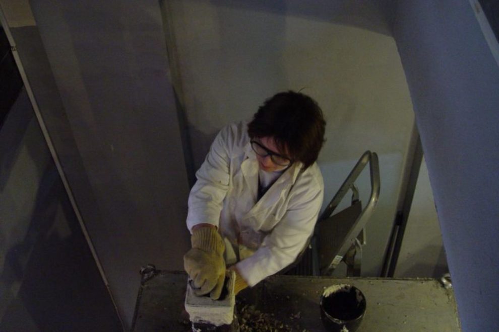 Researcher in lab coat operating an ancient pottery kiln replica during experimental archaeology work. 