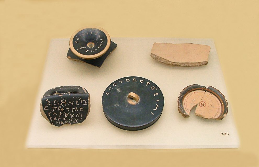 Fragments of ancient Greek pottery with inscriptions (kylix, skyphos, pyxis lid, amphora sherd with Greek alphabet), photographed at the Ancient Agora Museum in Athens.